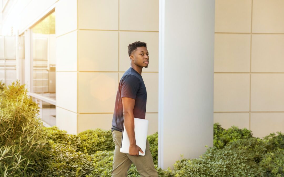 man holding laptop walking towards building